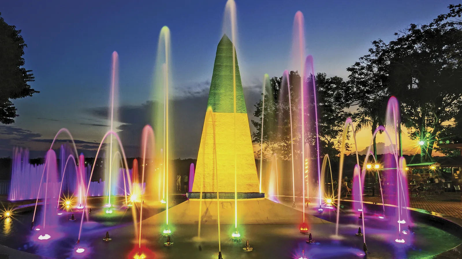 Marco das Três Fronteiras iluminado ao entardecer com fontes coloridas, em Foz do Iguaçu